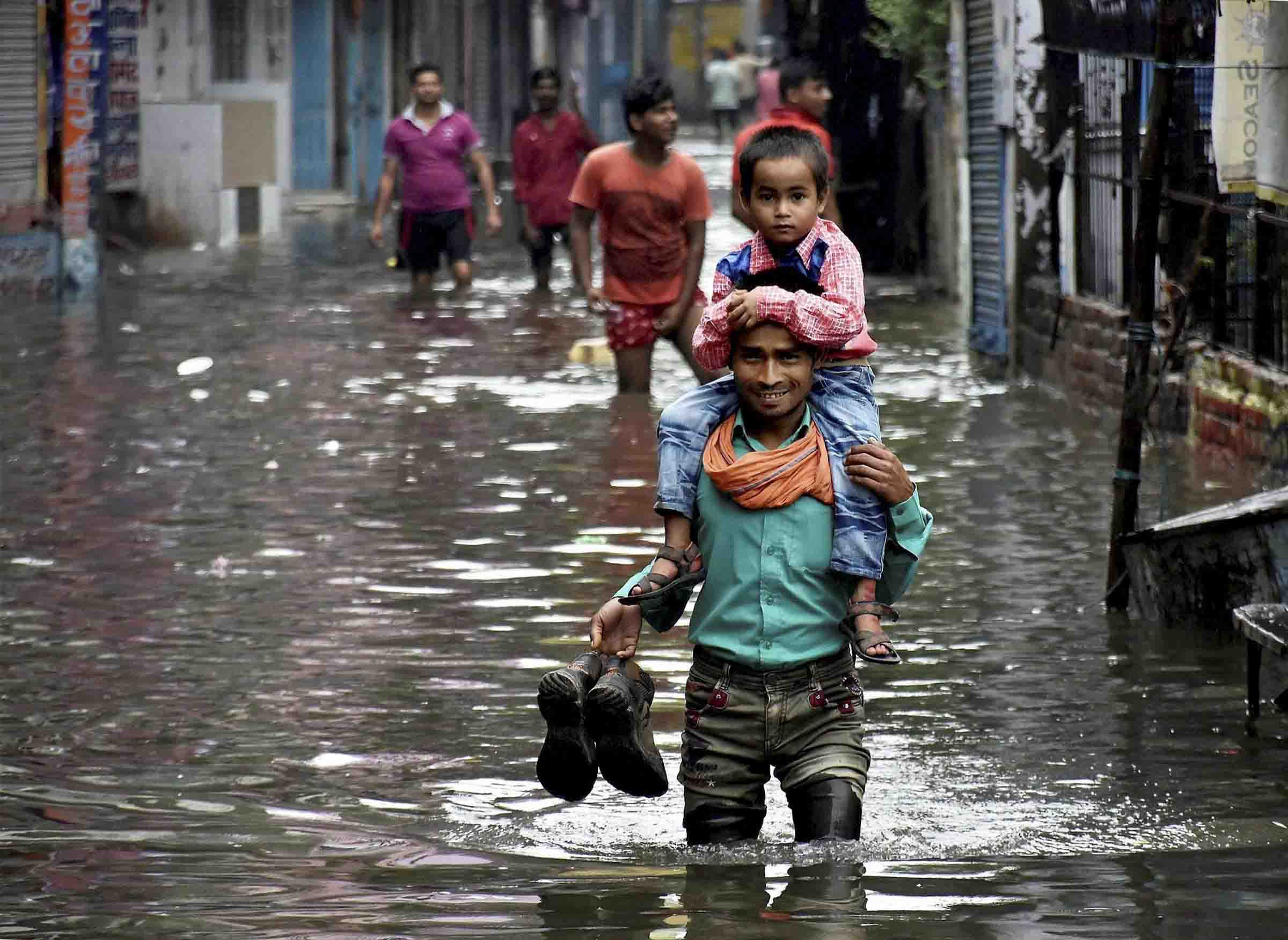 People wade through a water logged street after heavy rain in Patna on ...