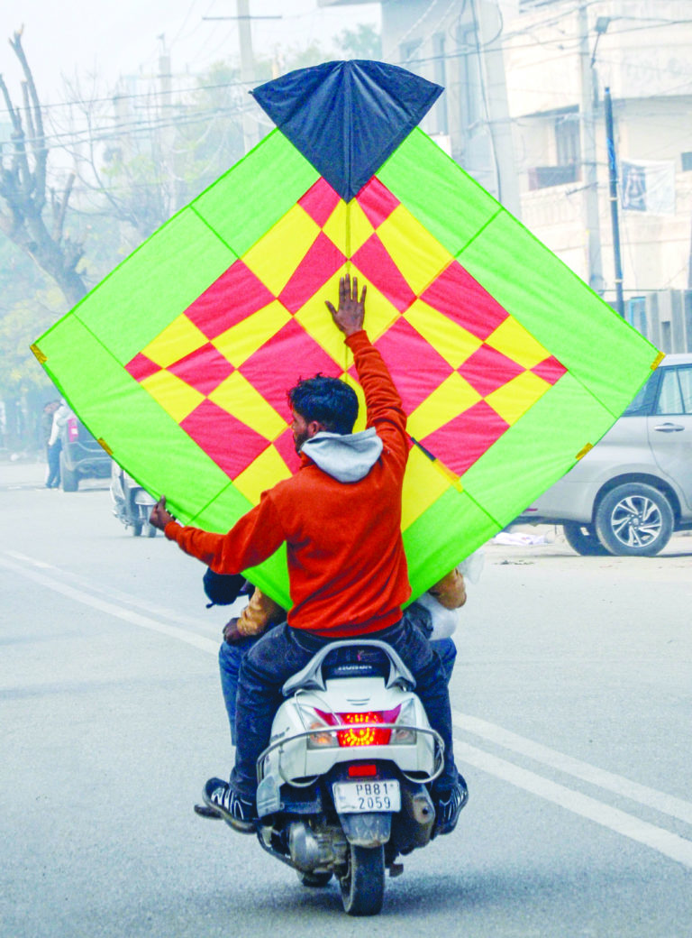 A man carries a large kite on a bike on the eve of Lohri.