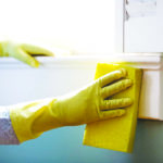 Woman using a damp sponge to clean dust collected on a window si